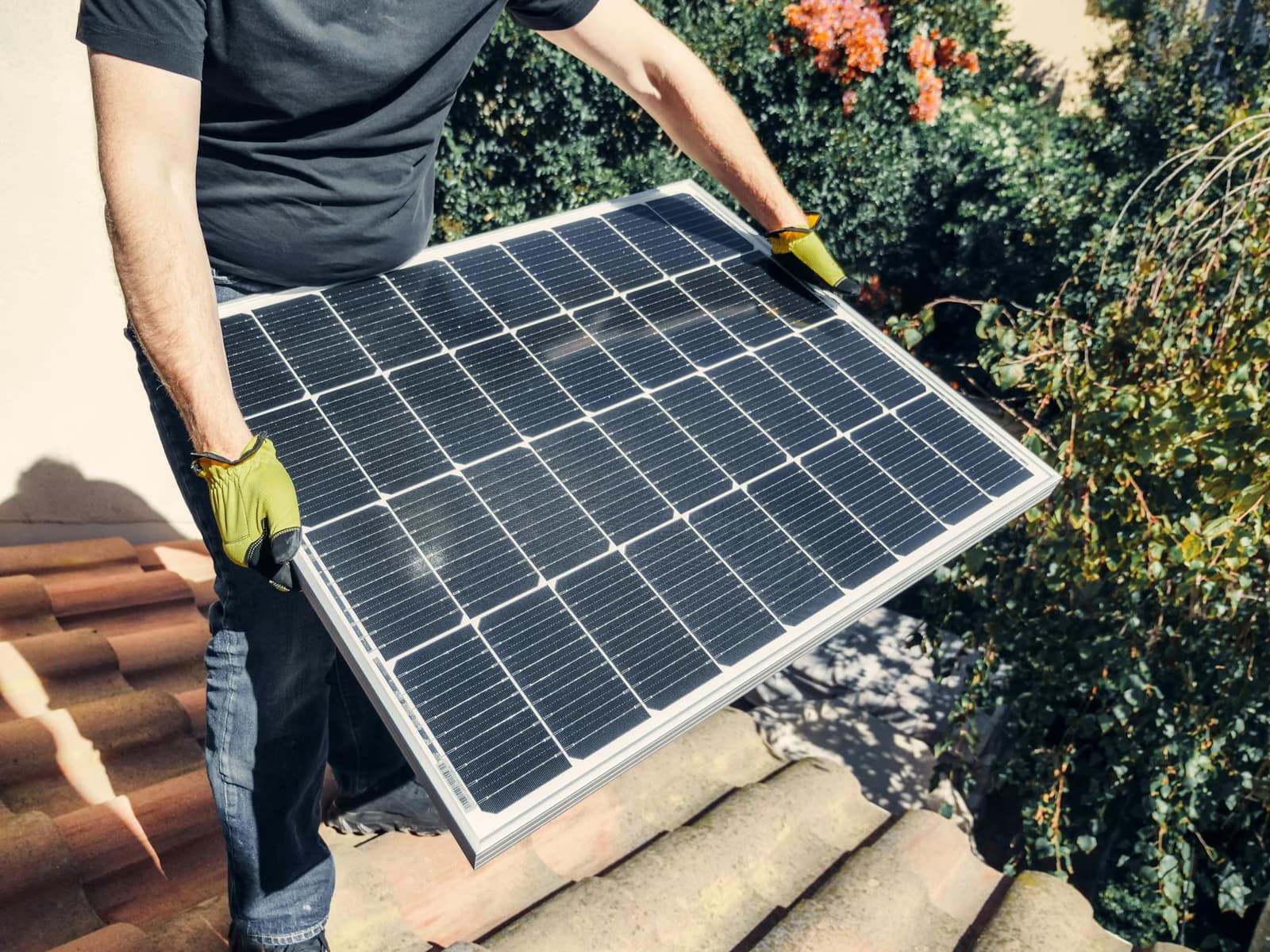 Personne portant des gants jaunes installant un panneau solaire photovoltaïque sur un toit en tuiles d'une maison de Saône-et-Loire au soleil