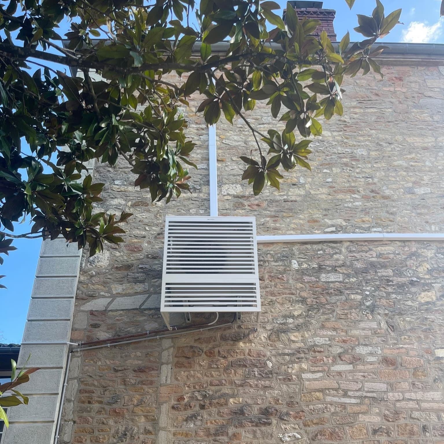 Outdoor air conditioning unit neatly concealed on the stone facade of a house near Chalon-sur-Saône