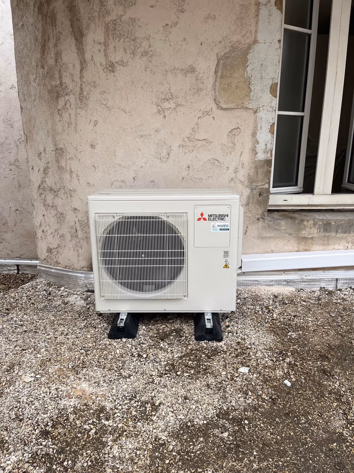 Unité extérieure de climatisation réversible Mitsubishi multi-split installée par Kozéo contre un mur en pierre à Dijon
