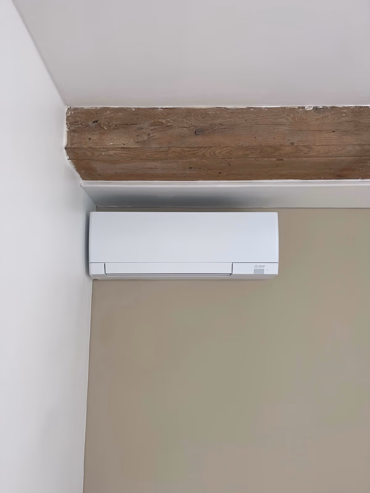 Unité intérieure murale de climatisation réversible Mitsubishi installée par Kozéo à Dijon, sous une poutre en bois