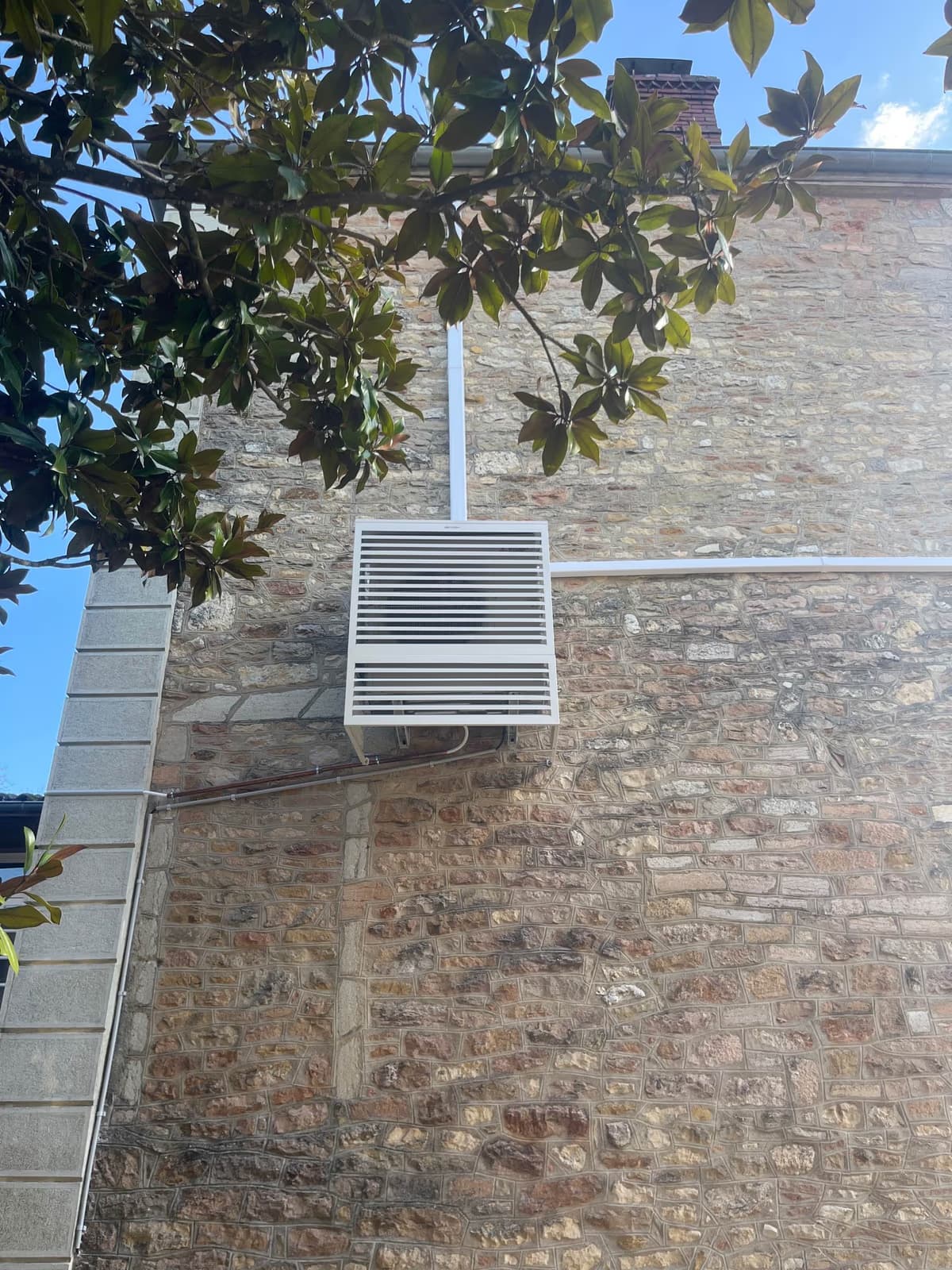 Cache-clim à lames blanches posé par Kozéo sur un mur en pierre à Prissé